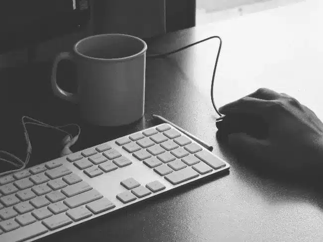 Hand using mouse next to computer and mug